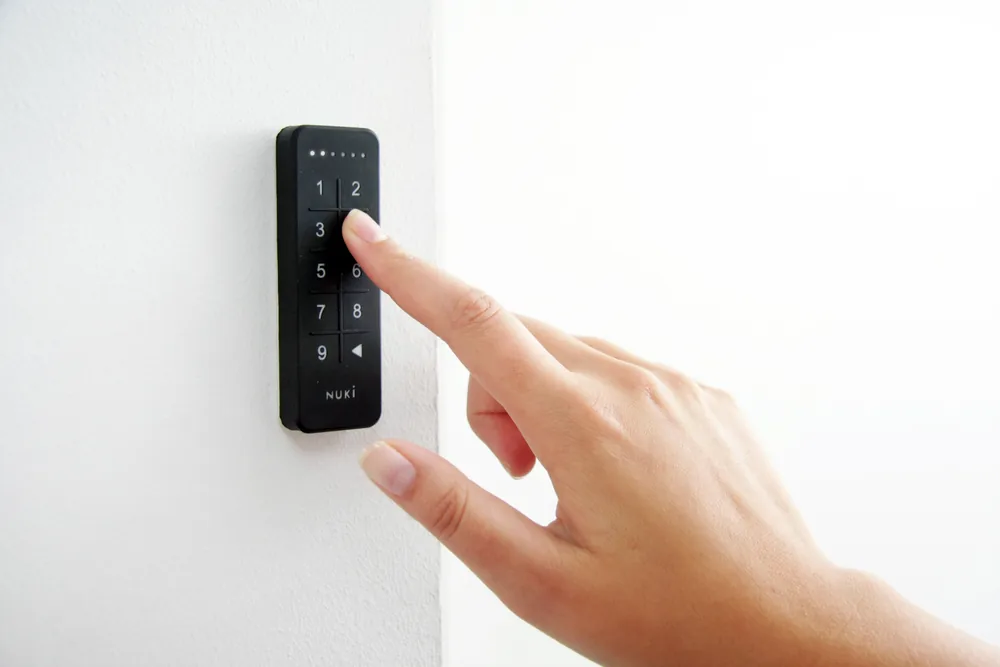 Dito che digita il codice sul Nuki Keypad fissato a una parete bianca