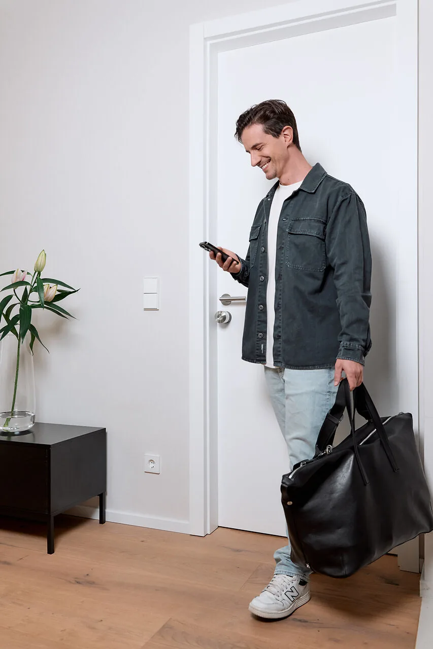 Uomo che rientra da una porta bianca con Smart Lock Pro guardando lo smartphone